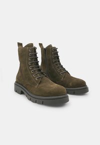 Botine din suede maro, cu vârful rotunjit, talpă din cauciuc negru, șapte ochiuri metalice și un fermoar pe lateral pentru o purtare ușoară.