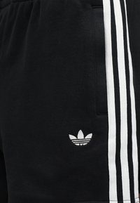 Μαύρο αθλητικό σορτς με λευκή τριπλή ρίγα στο πλάι και μικρό λευκό λογότυπο Adidas trefoil κοντά στην τσέπη.