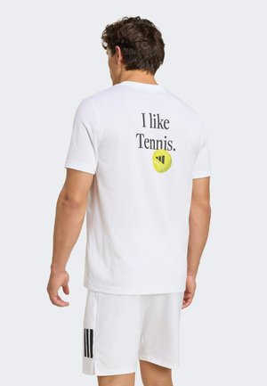 Mann trägt weißen Tennisanzug mit dem Text „Ich mag Tennis.“ und einer gelben Tennisball-Grafik auf der Rückseite des Shirts.