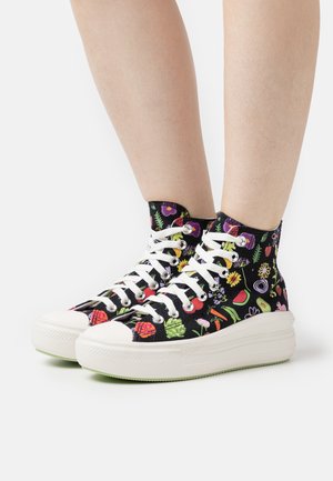 Højtop sneakers med et overdel i sort stof, der har et farverigt blomster- og frugtmønster. Hvide snørebånd og en tyk hvid sål med grønne detaljer.