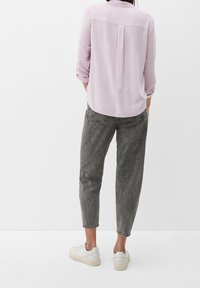 Camicia viola chiaro a maniche lunghe con una piega sulla schiena, abbinata a pantaloni grigi a vestibilità ampia. Le sneakers bianche completano il look.