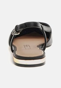 Black sandal with a textured upper, adjustable buckle, and low heel. Features a gold accent on the sole and a smooth insole with branding.