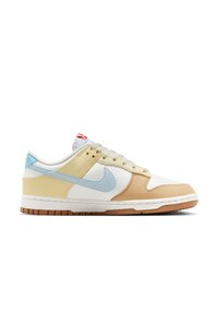Zapatilla Nike de corte bajo con paneles en blanco, beige, azul claro y marrón, swoosh azul claro y logotipo rojo en la lengüeta blanca.