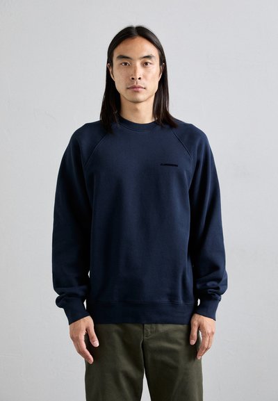 Sweatshirt bleu marine avec un col rond, des manches raglan et des poignets côtelés. Présente un logo subtil à l'avant. Texture de tissu douce.