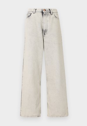 Szerokie dżinsy w jasnym beżowym kolorze z wyblakłymi, postrzępionymi akcentami. Posiada pięć kieszeni oraz metalowy guzik na zapięcie w pasie.