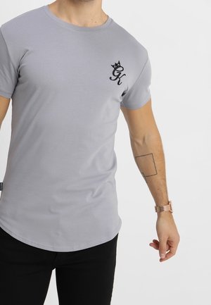 T-shirt gris à manches courtes en matière douce, avec un logo noir sur la partie gauche de la poitrine et un ourlet incurvé.