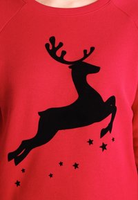 Felpa rossa con una grande silhouettes nera di una renna in salto, accentuata da piccole stelle nere sotto il design, realizzata in tessuto morbido.