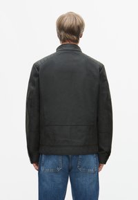 Czarna skórzana kurtka z pikowanymi akcentami na ramionach, o prostym kroju i kołnierzu. Noszona z niebieskimi dżinsami. Gładka tekstura, minimalne detale.