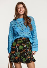 Maglione blu lavorato a maglia, con maniche lunghe e motivo traforato, abbinato a una gonna nera con motivo foglia tropicale e orlo ruffled.
