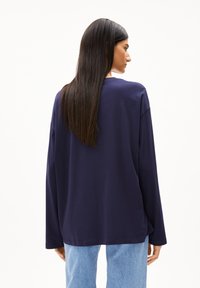 Marineblaue Langarmbluse aus weichem Baumwollmaterial mit einem lässigen Schnitt, abgerundetem Ausschnitt und seitlichen Schlitzen, kombiniert mit hellblauen Jeans.