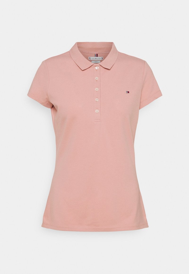 Damska koszulka polo z krótkim rękawem w kolorze przykurzonego różu z kołnierzykiem, pięcioma białymi guzikami i małym logo Tommy Hilfiger po lewej stronie klatki piersiowej.