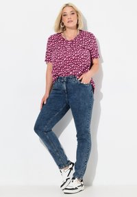 Vaaleanpunainen lyhythihainen paita, jossa on sydänkuvio, yhdistettynä sinisiin kapealahkeisiin farkkuihin ja musta-valkoisiin lenkkareihin, klassinen tyyli ja hienovaraiset tekstuurit.