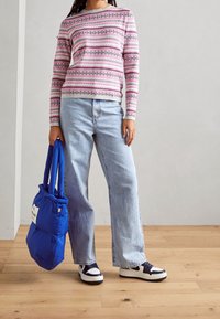 Pull léger rose à motifs avec des manches longues, associé à un jean bleu ample. Tenant un sac fourre-tout bleu. Baskets avec des accents blancs et marine.