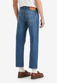 Vaqueros azules de mezclilla con corte recto, diseño de cinco bolsillos y una etiqueta de cuero marrón claro en la cintura trasera. Presentan un lavado ligeramente descolorido.