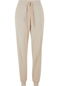 Beige joggebukser laget av mykt materiale, med strikket liv med snor og ribbede mansjetter ved ankelen.