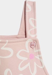 Rosa gemusterter Jumpsuit mit weißem Blumenmuster, ausstattet mit verstellbaren Trägern und einem pinken Knopfdetail an der Schulter. Weicher Stoff.