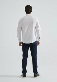 Chemise blanche à manches longues avec des poignets à boutons, assortie à un pantalon bleu foncé. La chemise présente un col classique et une texture en coton lisse.