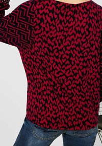 Röd och svart mönstrad topp med leopardtryck, texturerat tyg och kontrasterande geometriska mönster på ärmarna. Avslappnad passform.