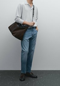 Jasnoszara koszulka polo z długim rękawem, niebieskie dżinsy i czarne buty na sznurowadła, w towarzystwie ciemnobrązowej torby z skórzanymi akcentami.