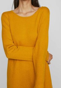 Senapsgul långärmad stickad tröja med bred båtkrage. Mjuk textur och avslappnad passform, med ribbade ärmslut och nederkanter.