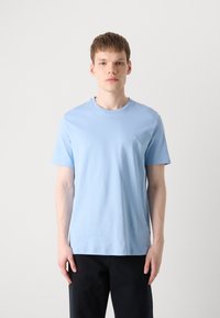 Light blue cotton t-shirt with a crew neckline, short sleeves, and a small logo on the chest, paired with dark pants.