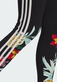 Černé legíny s barevnými tropickými květinovými vzory, bílými pruhy po stranách a hladkým, elastickým materiálem.