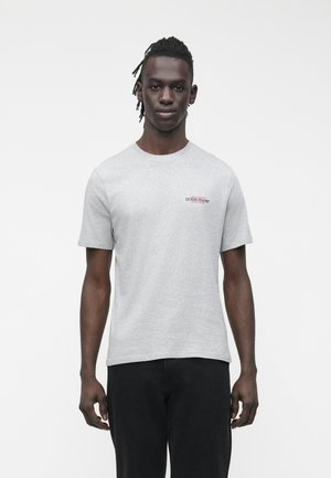 Graues Baumwoll-T-Shirt mit kurzen Ärmeln und kleinem roten und schwarzen "GUESS JEANS"-Logo auf der linken Brust. Legere Passform und rundem Ausschnitt.