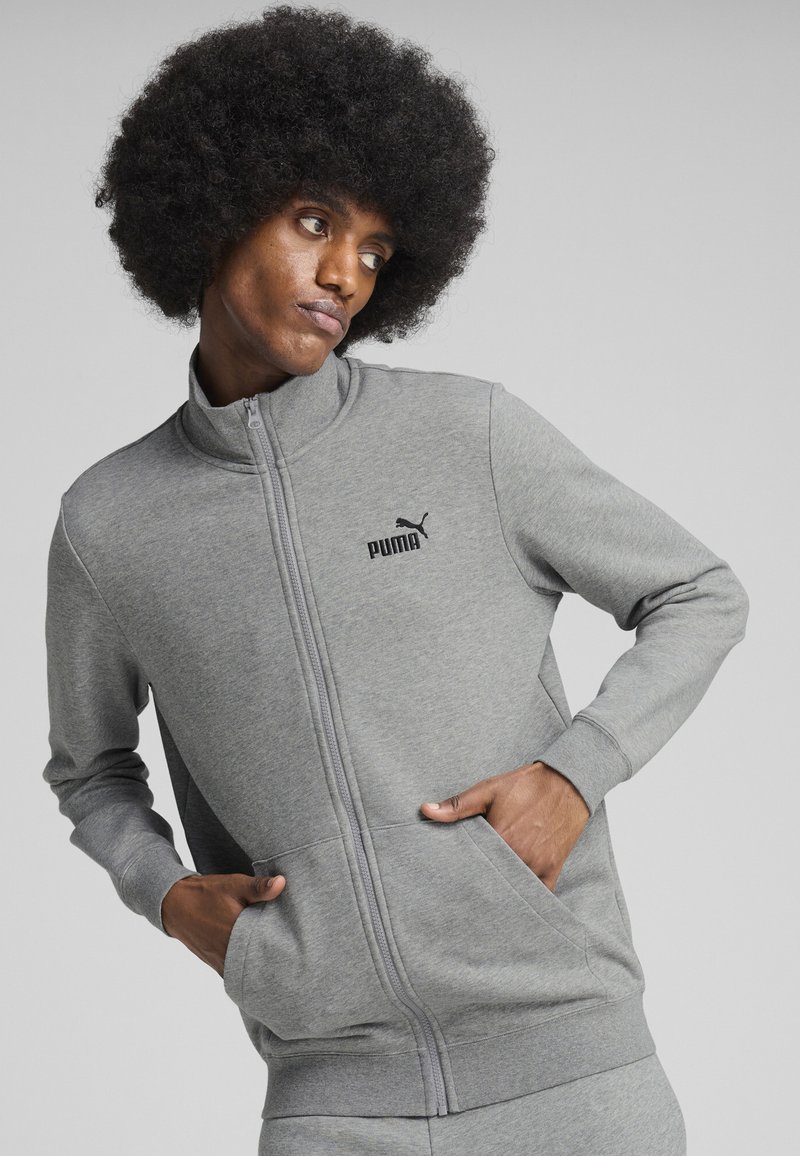 Šedá zipsová mikina s vysokým golierom, ktorá má bočné vrecká a čierne logo Puma na hrudi. Mäkká tkanina, predĺžené rukávy, minimalistický dizajn.