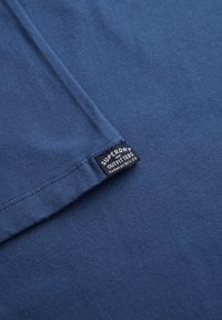 T-shirt bleu marine à manches courtes, fabriqué en coton doux, avec une étiquette tissée sur l'ourlet portant le logo "Superdry".
