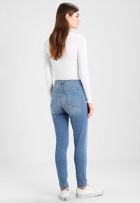 Jeans skinny de denim azul con cintura alta y bolsillos traseros, combinados con una camiseta de manga larga blanca y zapatillas blancas.
