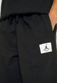 Schwarze Baumwoll-Jogginghosen mit elastischem Taillenbund, seitlichen Taschen und einem weißen Etikett mit einem schwarzen Jumpman-Logo auf dem Oberschenkel.