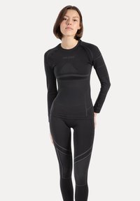 Czarny sportowy zestaw składający się z długiego rękawa i dopasowanych legginsów. Wykonany z gładkiego, elastycznego materiału z subtelnymi akcentami wzoru.