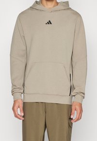 Hoodie di un beige chiaro con tasca a marsupio, polsini a coste e un piccolo logo nero sul petto. Presenta una vestibilità casual e rilassata.