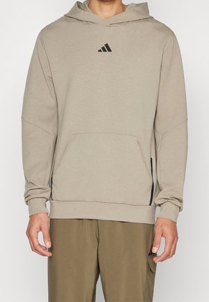 Hoodie beige claro con bolsillo tipo canguro, puños acanalados y un pequeño logo negro en el pecho. Presenta un ajuste casual y relajado.