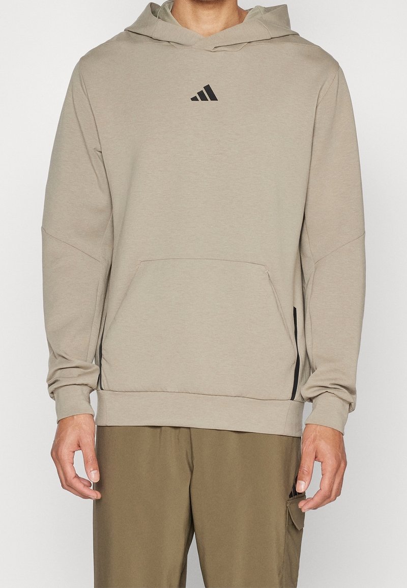 Hoodie di un beige chiaro con tasca a marsupio, polsini a coste e un piccolo logo nero sul petto. Presenta una vestibilità casual e rilassata.