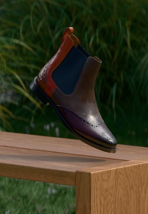 Herren Leder Chelsea-Boot mit Brogue-Details in Braun, Burgunder und Hellbraun, schwebend über einer Holzbank im Freien.
