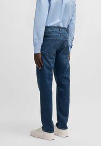 Mörkblå denimjeans med rak benklippning, med bakfickor och en lätt fade. Stylen kombineras med en ljusblå skjorta och vita sneakers.