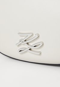 White leather pouch featuring a prominent silver logo with intertwined accents. Smooth texture, minimalistic design, rounded shape.