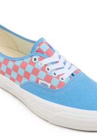 Zapatillas de lona azules con un patrón de tablero de ajedrez en rosa y azul, cordones blancos y suela de goma. Logo "VANS" notable en el lateral.
