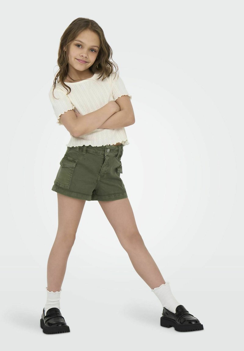 Vit ribbad kortärmad topp och olivgröna cargoshorts med framfickor. Svarta platåskor och vita volangankelsockor.