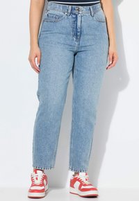 Helleblaue Jeans mit hoher Taille, geradem Schnitt, fünf Taschen und ausgefransten Säumen, kombiniert mit rot-weißen Turnschuhen.