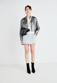 Giacca bomber grigia metallizzata, top bianco, gonna mini a righe con bottoni, borsa nera e stivali neri alla caviglia con punte appuntite.