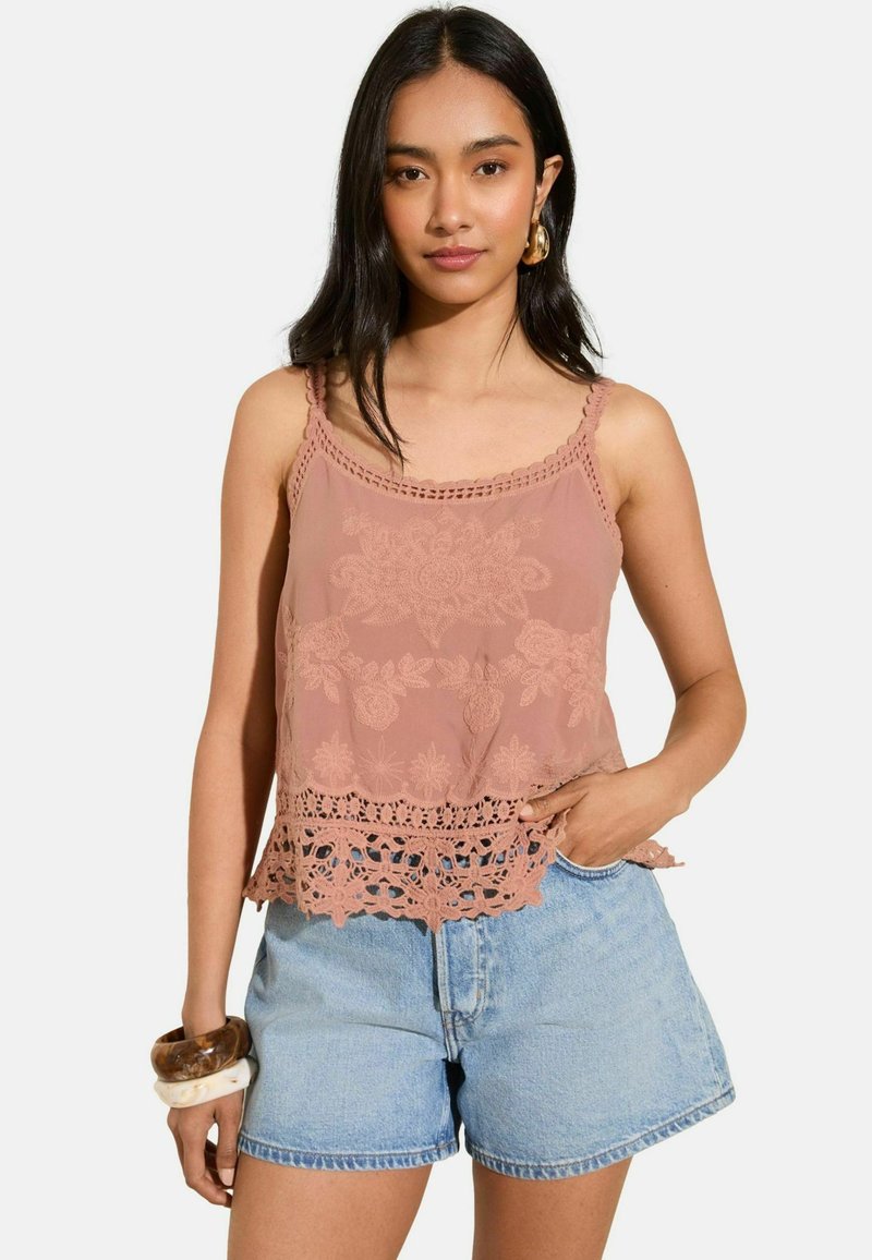 Top in rosa blush con ricami floreali e bordi in pizzo, abbinato a pantaloni corti di denim chiaro. Presenta spalline regolabili e una vestibilità ampia.