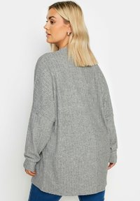 Grauer gerippter Pullover mit langen Ärmeln und lockerer Passform, ausgestattet mit einem weiten Ausschnitt und einem mittellangen Design aus strukturiertem Strickstoff.