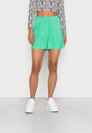 Shorts plissés vert menthe avec une taille élastique ; associés à un crop top à imprimé zèbre noir et blanc et à des baskets à plateforme blanches.