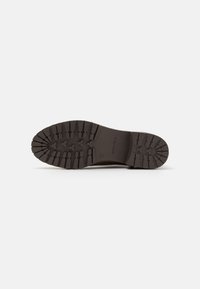 Suela de bota de goma marrón con patrón de textura en la banda de rodadura, tacos elevados para mayor agarre y detalle del logo en relieve en la entresuela.