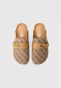 Paar lichtbruine instap loafers met monogrampatroon, leren riem en gouden gespdetail, met het label Guess op de gevoerde binnenzolen.