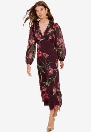 Long, burgundy floral dress with sheer long sleeves and a deep V-neck. Features a flowing design and bold pink and green floral patterns.