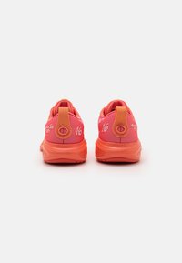 Baskets de sport roses avec un dessus en maille texturée, un col rembourré et une semelle en caoutchouc. Présente des accents orange contrastés et un marquage.