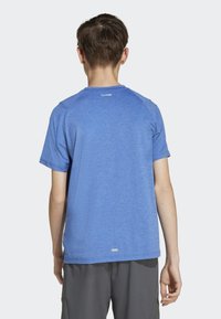 Modrá sportovní tričko s krátkým rukávem a texturovanou tkaninou; obsahuje raglánové rukávy a logo blízko límce, doplněné šedými šortkami.